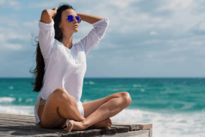 woman sitting cross legged on a beach, having manifested her dream life