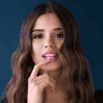 Young woman with long wavy hair against a deep blue background, touching her lip thoughtfully