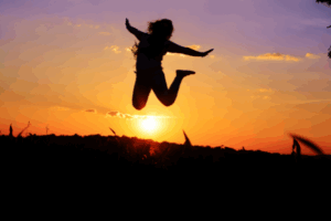 Silhouette of a joyful woman jumping against a vibrant sunset sky, symbolizing freedom and breakthrough