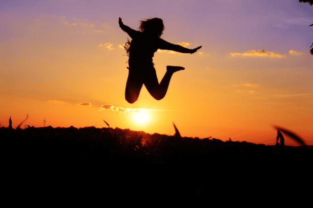 Silhouette of a joyful woman jumping against a vibrant sunset sky, symbolizing freedom and breakthrough