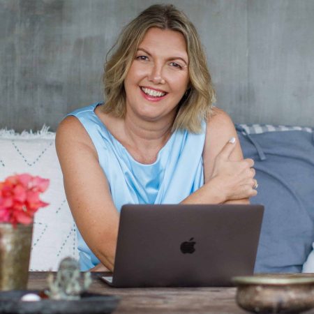 Kristina – Holistic Life Coach at Work Kristina smiling warmly while sitting at her laptop, offering online holistic life coaching.